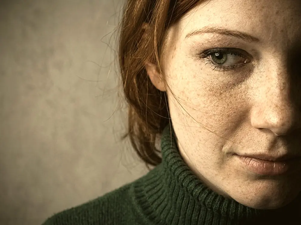 Close-up of a woman in a green sweater gazing ahead in resignation