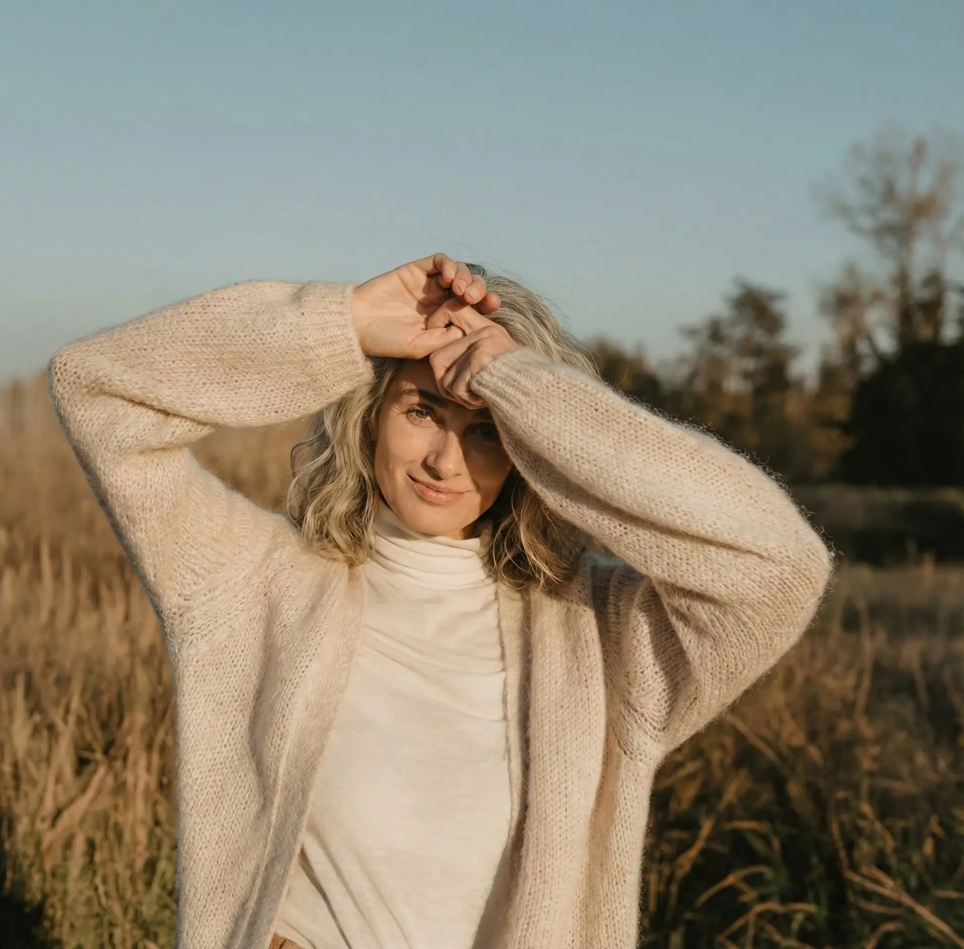 Woman in a sunny field in a cream cardigan, full of vitality