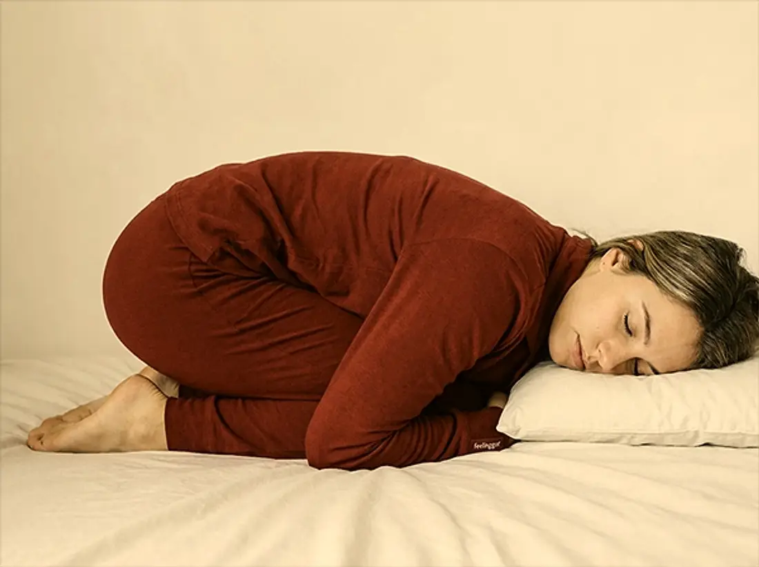 Woman lying curled up on a bed in warm light, exhausted but at rest